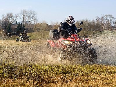 A quad bike being driven through a wet field, with another quad bike in the background