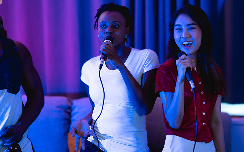 Two women singing karaoke into microphones 
