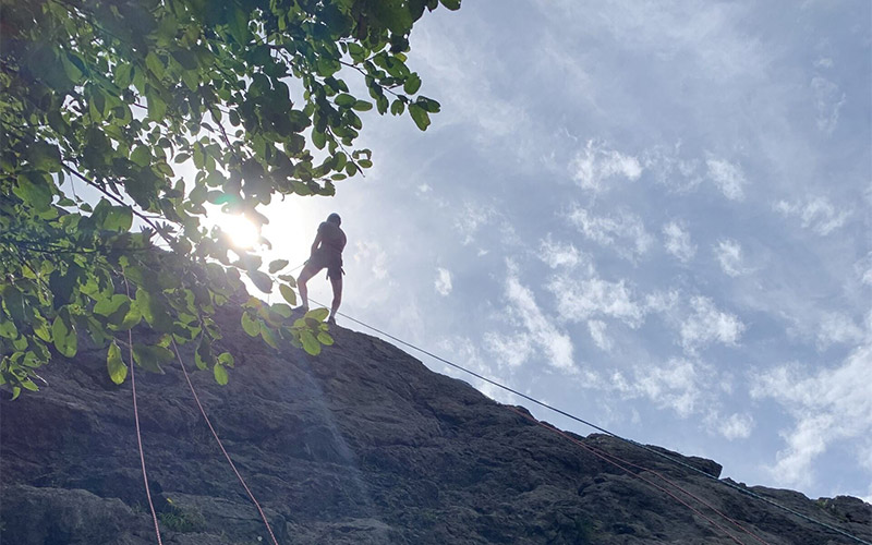 Someone rock climbing standing at the top of the rock cliff 