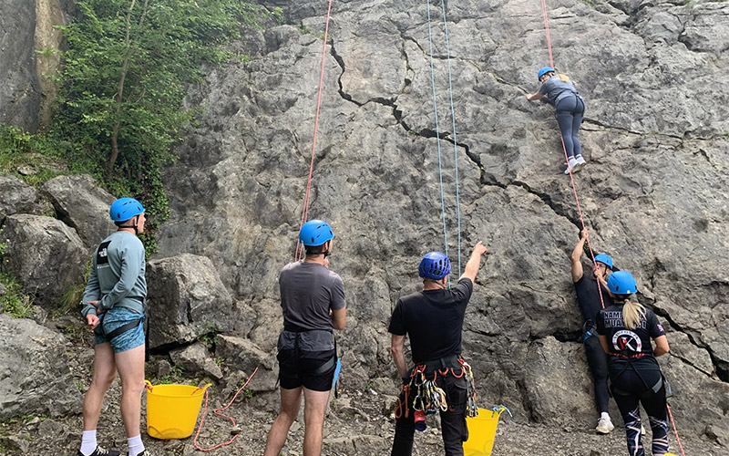 Someone rock climbing whilst being belayed by their team