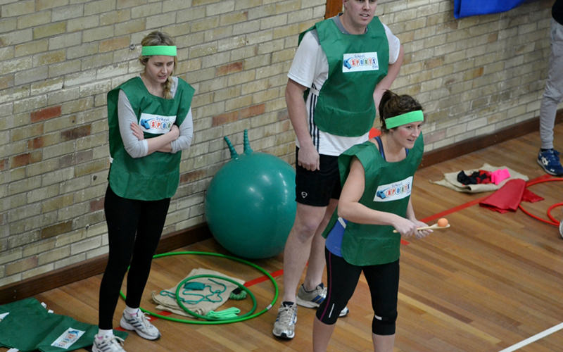  Two women and a man dressed in green vests in a sports hall
