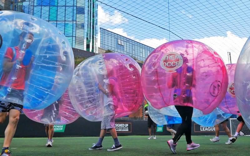 A large group of people playing bubble football in blue and red inflatable zorbs