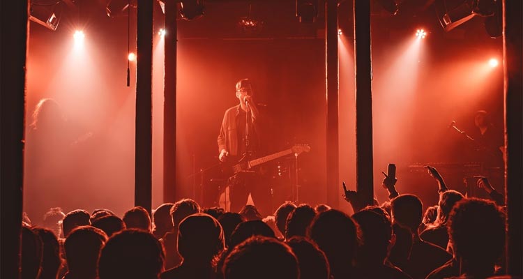 A large crowd of people watching a band in dim red lighting. 