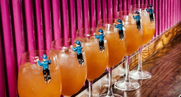 A line of aperol spritz drinks that each have a mini figure on the brim 