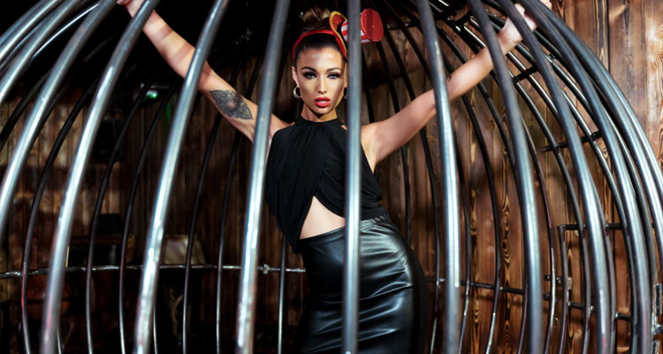 A woman in a leather skirt and black top posing in a black cage. 
