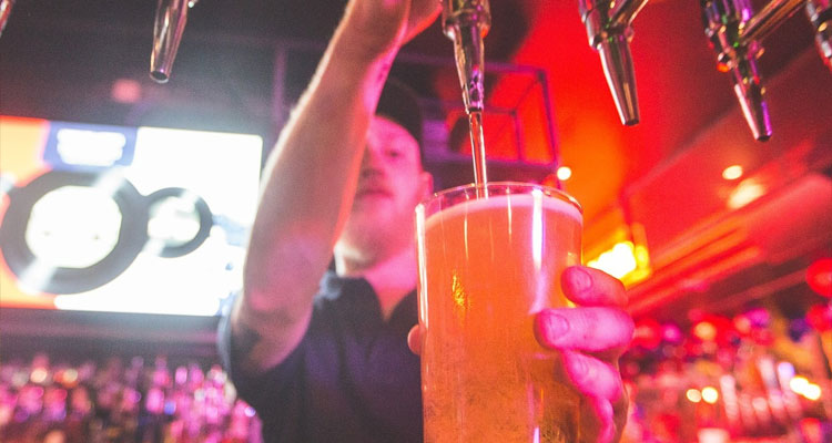 A male bar tender pulling a pint in the bar of Box in Manchester. 