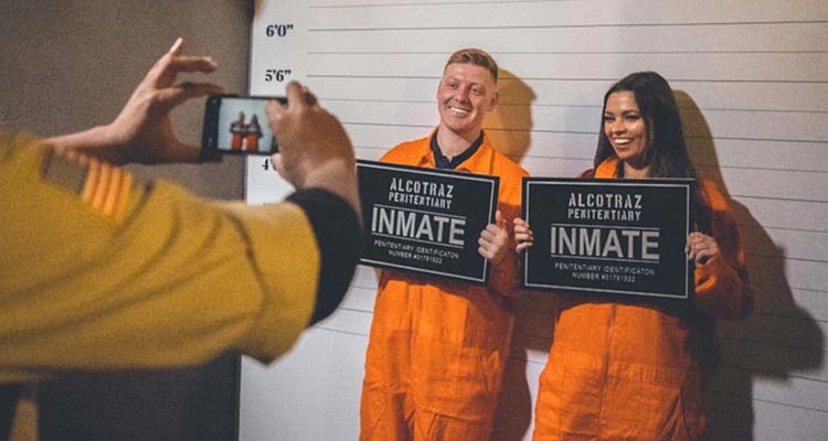 A man and a woman wearing orange jumpsuits holding signs that read Inmate. 