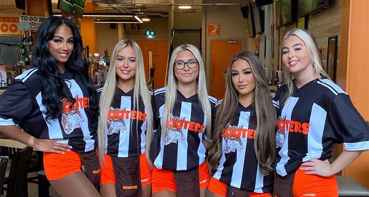 Five Hooters girls wearing hooters outfits with orange shorts and Newcastle United shirts with the Hooters logo 