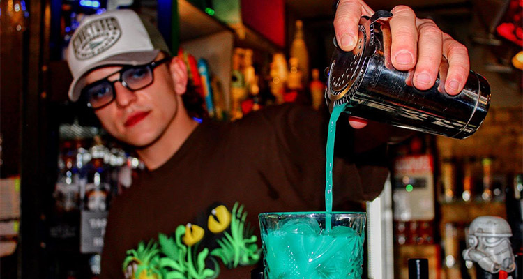 A bartender pouring a bright blue cocktail from a cocktail shaker at Clayton McNamaras Drinking Emporium