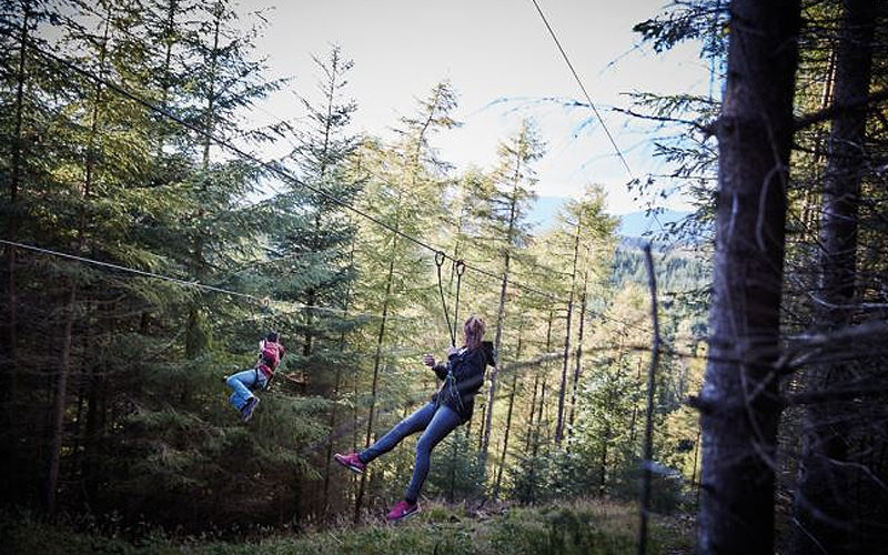Two girls zipwiring through the forest
