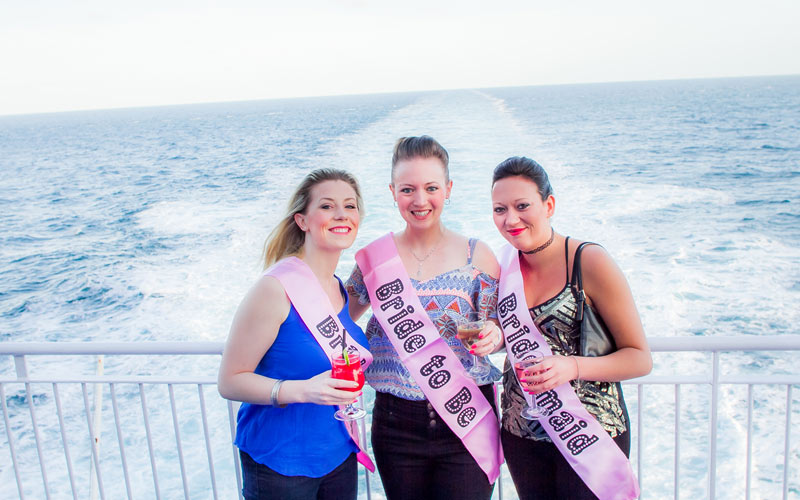 Some women wearing hen party sashes on the back of a boat