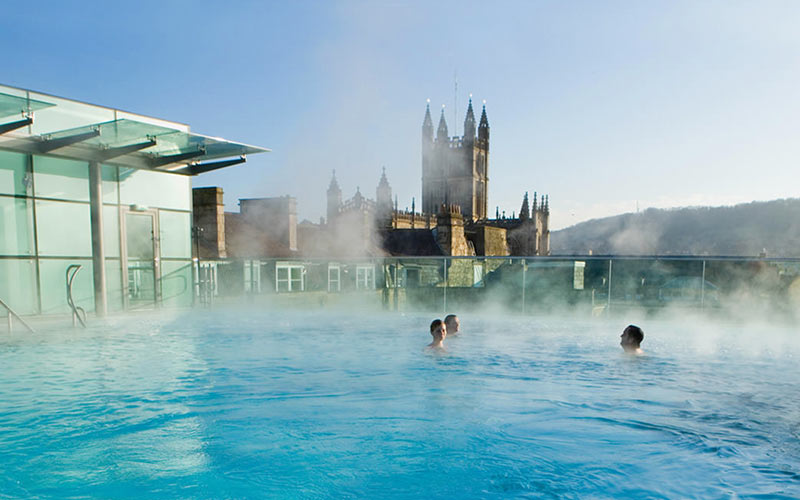 Some people in a medicinal bath overlooking the city of Bath
