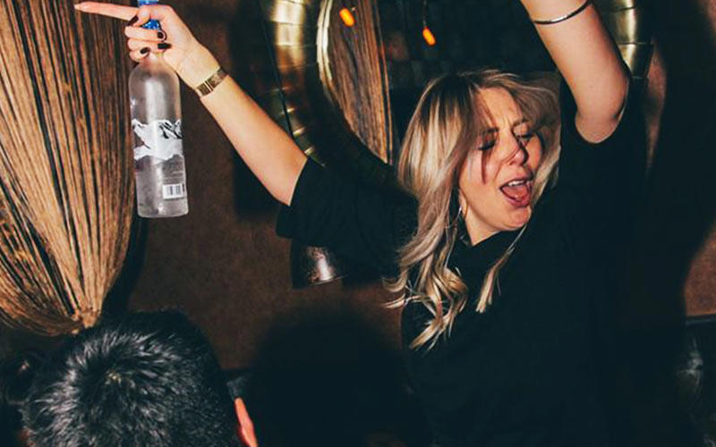 A girl holding a bottle of Grey Goose, with her arms in the air
