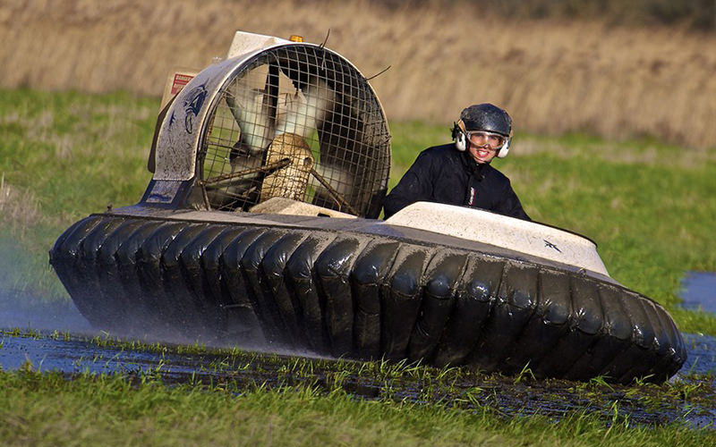 A woman riding on a hovercraft, across a wet field