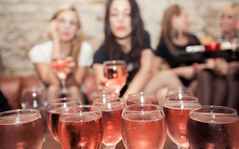 Some glasses of wine with some girls in the background