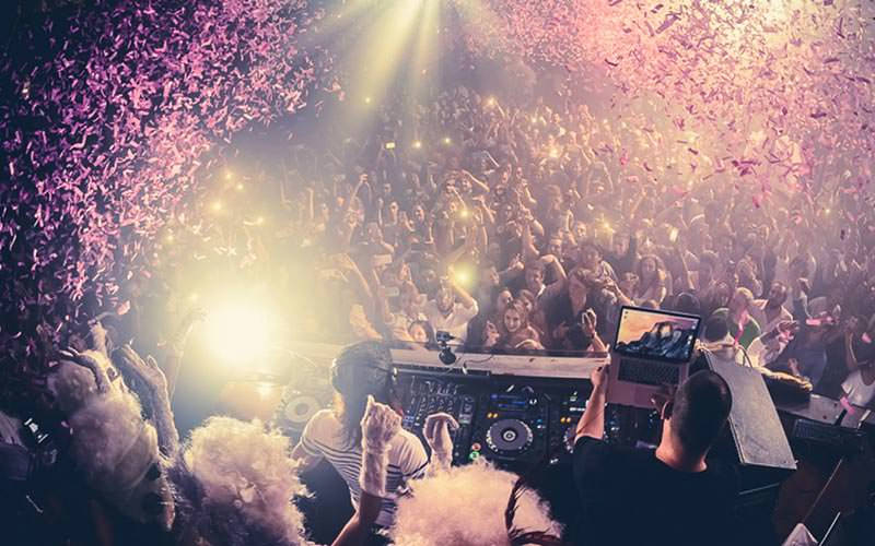 A DJ performing to a huge crowd, with pink tickitape coming down from the ceiling