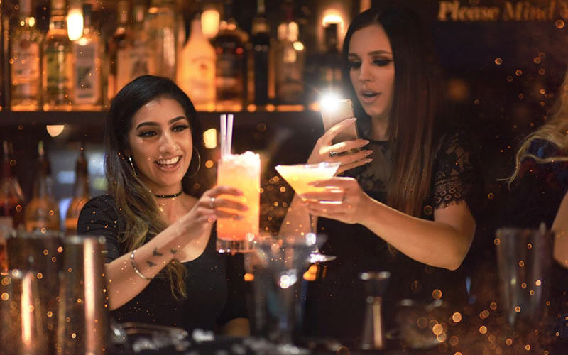 Two girls taking a photo of their cocktails in a bar