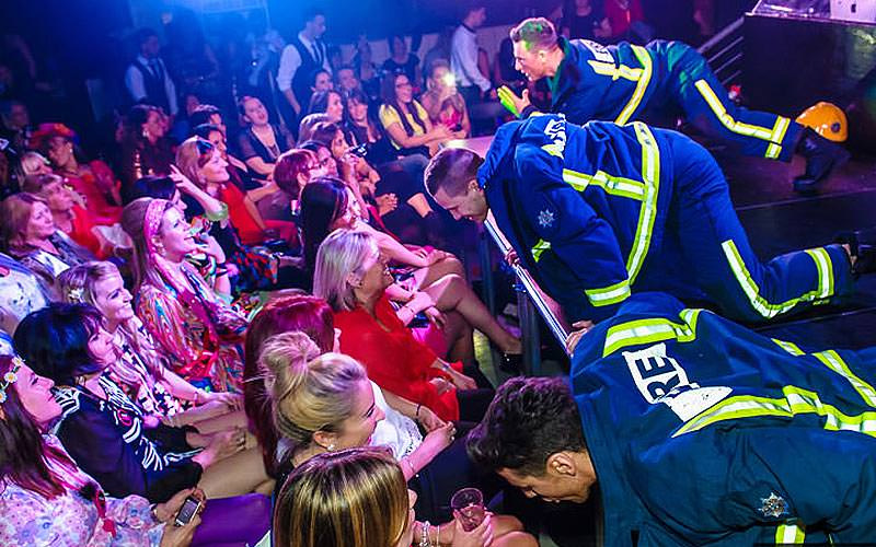 Some strippers dancing on stage wearing firemen's outfits