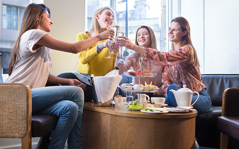 Four girls clinking their glasses together over afternoon tea 