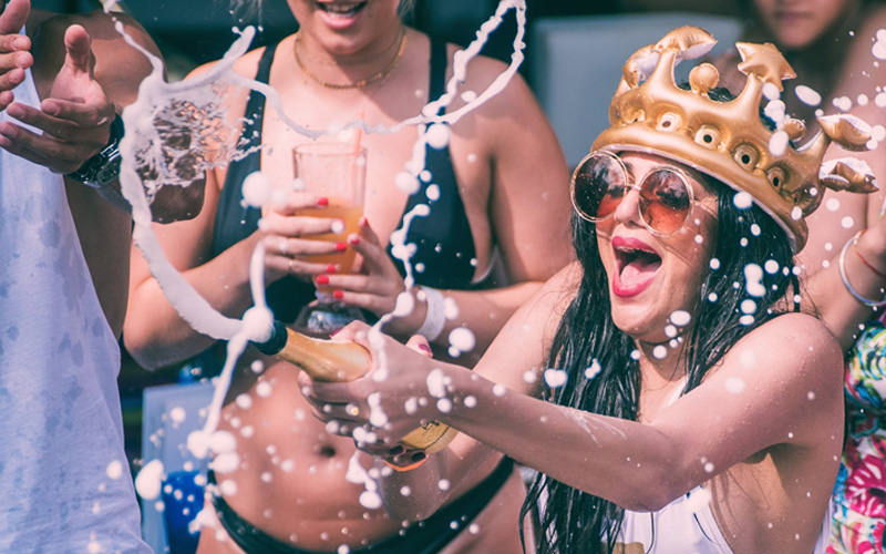 A girl wearing a crown, opening a champagne bottle
