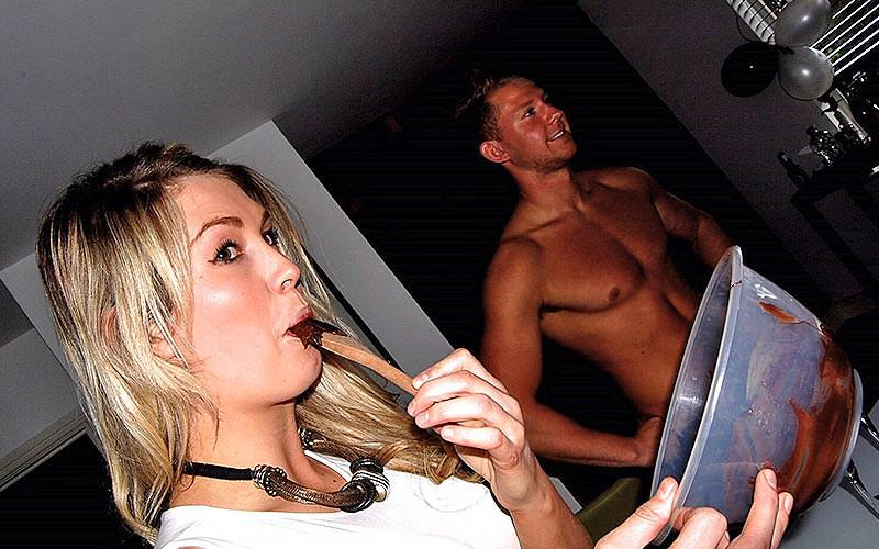 A girl eating chocolate from a bowl, with a topless man in the background