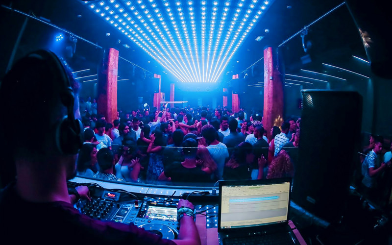 A group of people dancing in a club, with a DJ in the foreground
