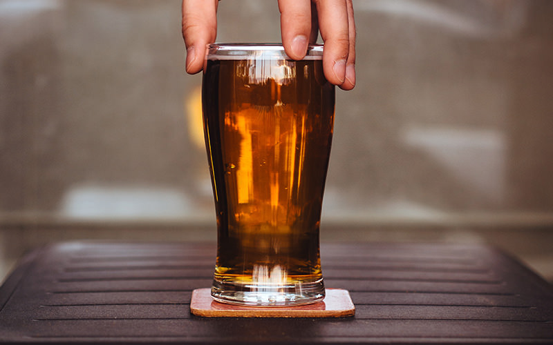 A man's fingertips holding the rim of a pint