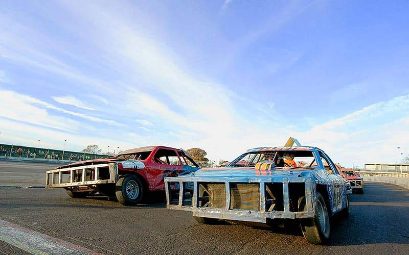 Two battered old cars in a car park, with modified bumpers