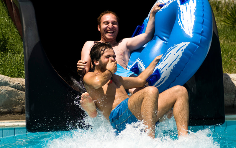 Two men coming down a flume into a a swimming pool
