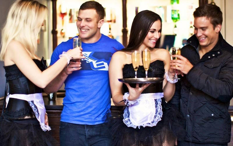 Some sexy butlerettes serving prosecco to some men