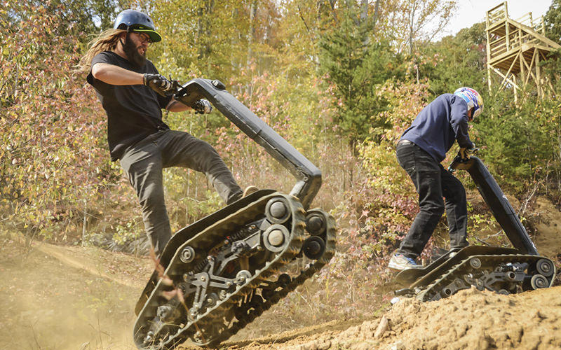 Two men on segways, riding over a dirt track