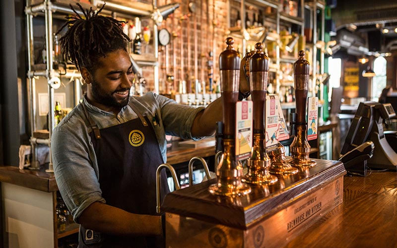 A barman pulling a pint in a hipster bar
