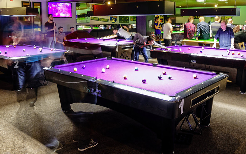 Some people playing pool on tables with purple felt