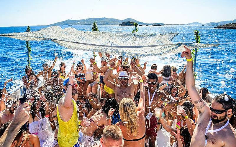 A group of young people on a boat, holding drinks up in the air