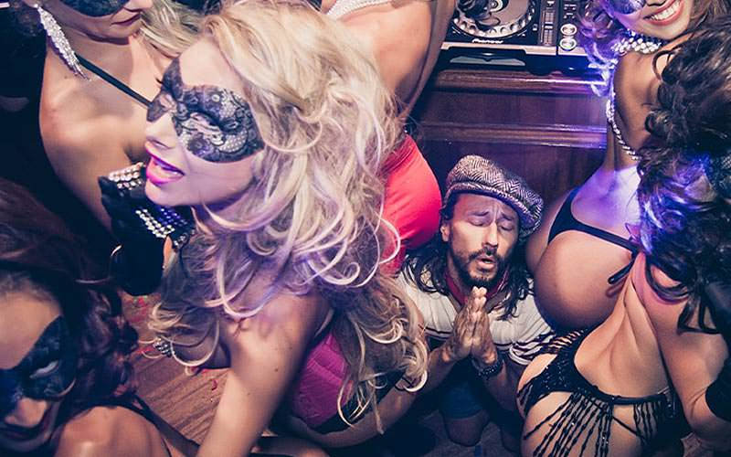 A man saying a prayer as he kneels on the floor and many women grind on him