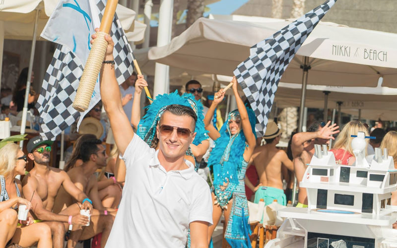 A man holding his arm in the air and some girls behind holding racing flags
