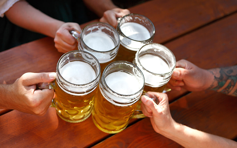 Five steins clicking together in a cheers position, over a wooden table