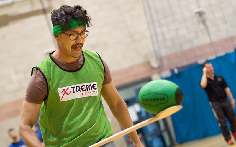 A man balancing a rugby ball on a wooden spoon while running