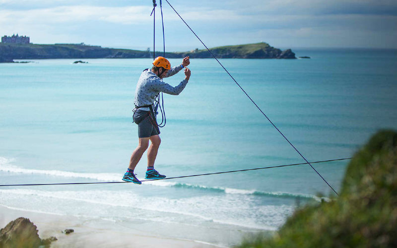 A man doing a tightrope walk in Newquay, with the stunning scenery as a backdrop