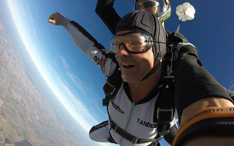 Two people sky diving, with a parachute opening out above them