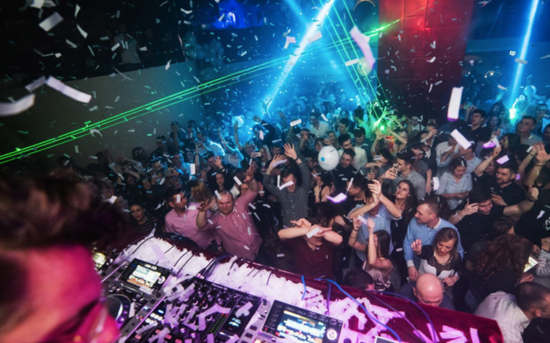 A group of people dancing in a club with strobe lights of various colours