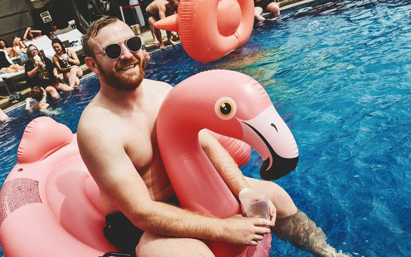 A man sat on an inflatable pink flamingo, in a swimming pool