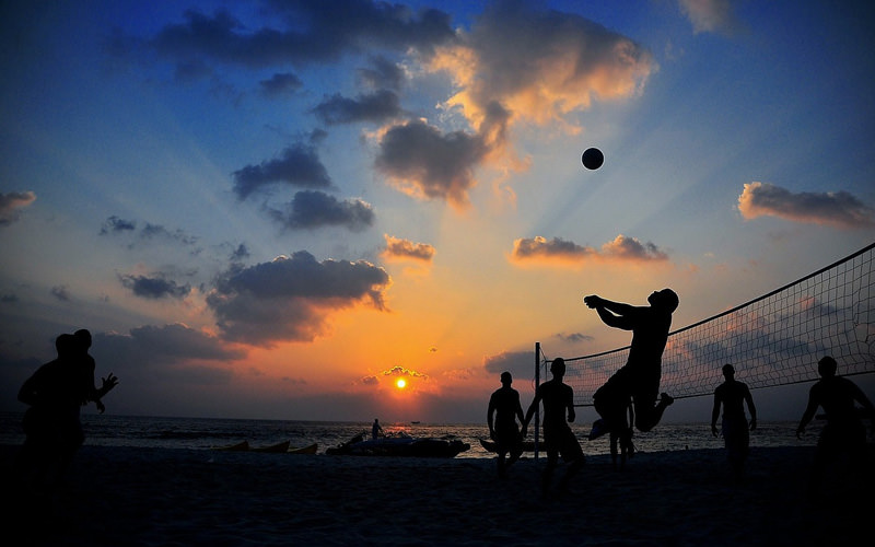 A group of people playing beach volleyball at sunset