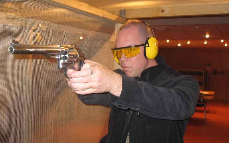 A man wearing protective ear guards aiming a gun