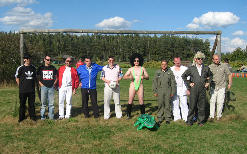 A group of men stood in front of a football goal outside, with one dressed in a green mankini