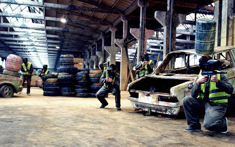 A group of people in high visibility vests crouching and hiding, carrying paintball guns
