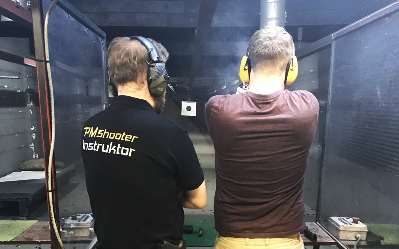 The back of a man's head, wearing protective ear guards aiming at a target