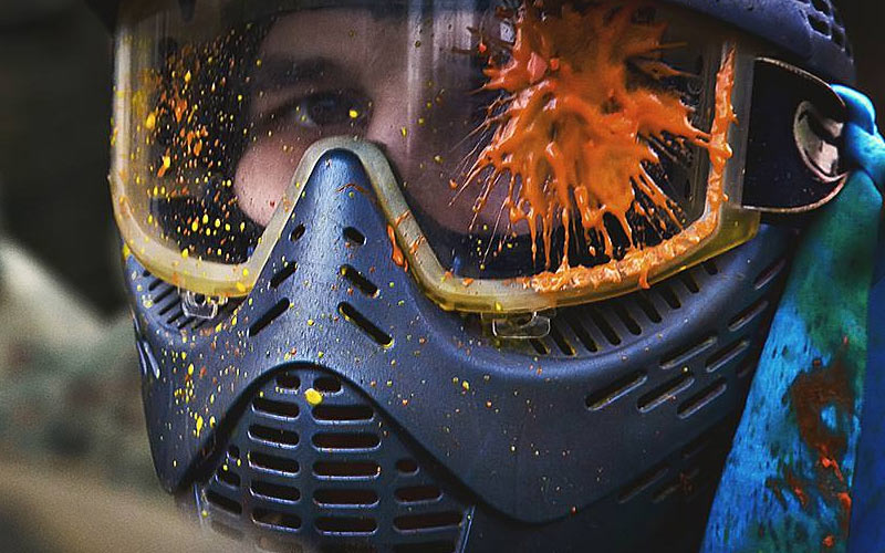 A close up of a paintball helmet with some splattered paint on