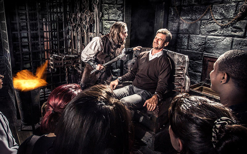 A group of people watching a man in a torture room, in York dungeons
