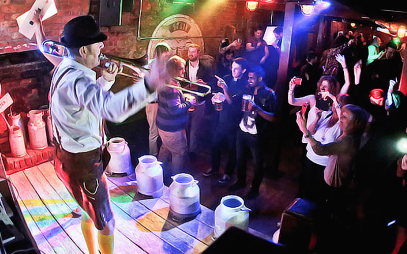 A group of people dancing to a man stood on a table, playing a trumpet